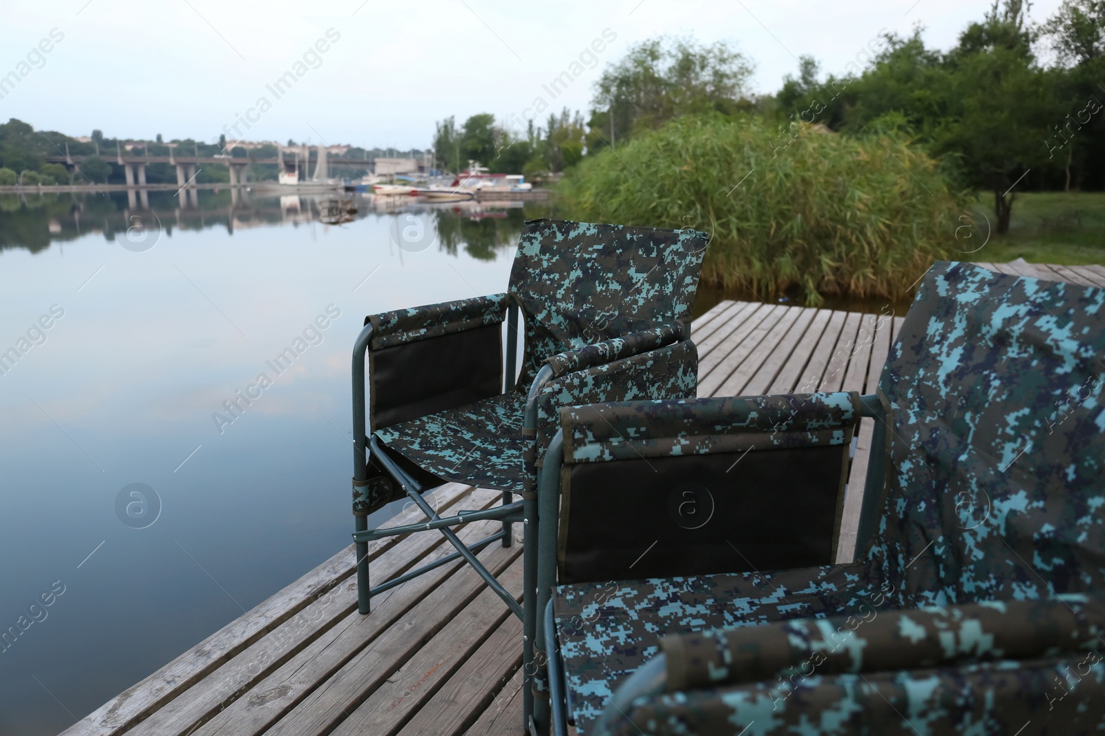 Photo of Camouflage fishing chairs on wooden pier near river