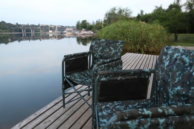 Camouflage fishing chairs on wooden pier near river