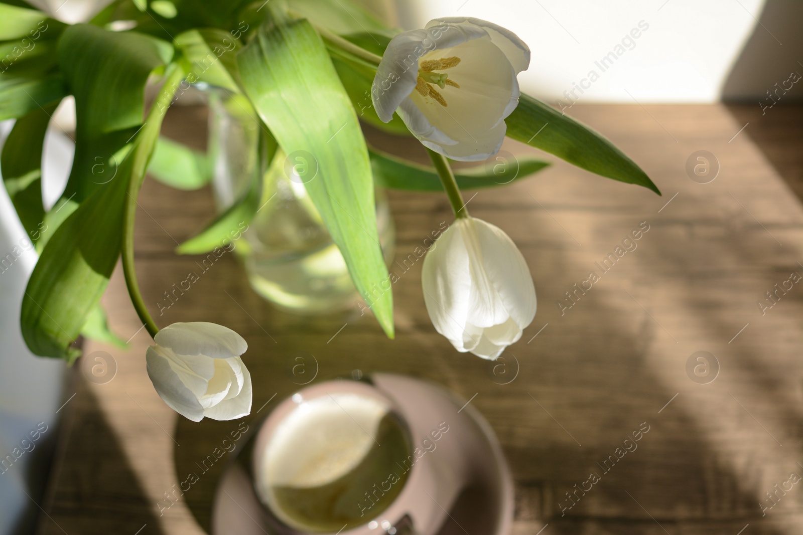 Photo of Beautiful white tulip bouquet and cup of coffee indoors, focus on flowers