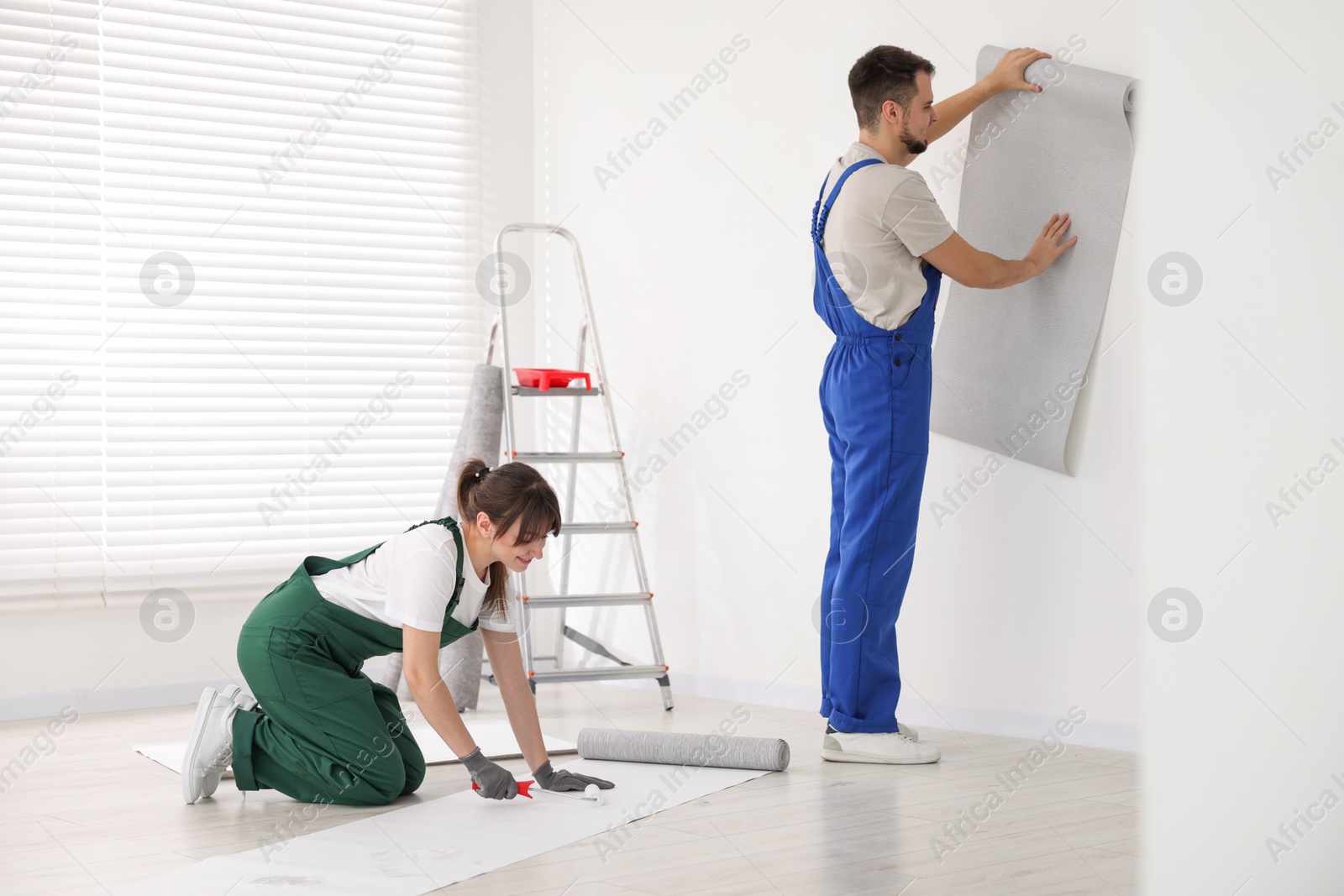 Photo of Woman applying glue onto wallpaper while man hanging sheet indoors