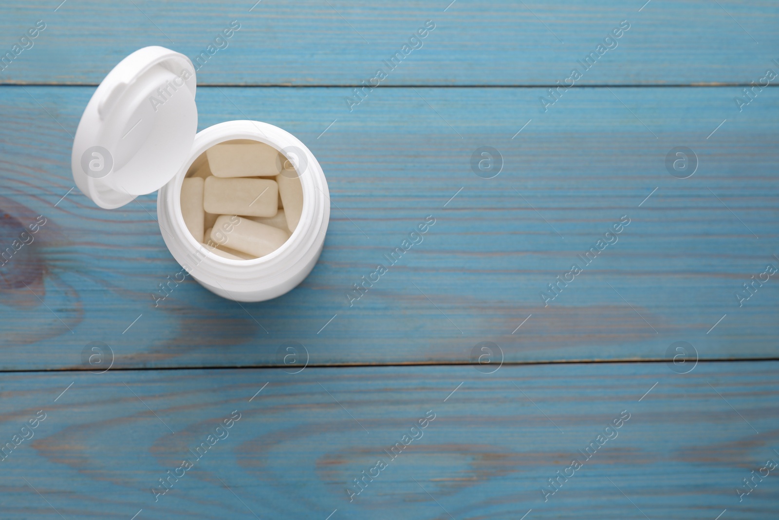 Photo of Jar with chewing gums on light blue wooden table, top view