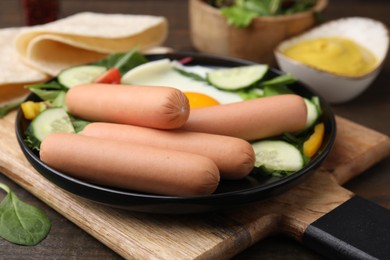 Delicious breakfast with boiled sausages and fried egg on wooden table, closeup