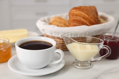 Breakfast time. Fresh croissants, coffee, jam, honey and sweetened condensed milk on white table, closeup