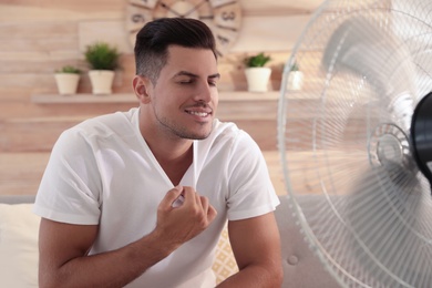 Man enjoying air flow from fan on sofa in living room. Summer heat