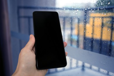 Woman holding smartphone with blank screen near window, closeup