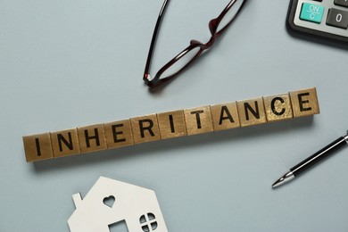 Photo of Word Inheritance made with cubes, house model and pen on light blue background, flat lay