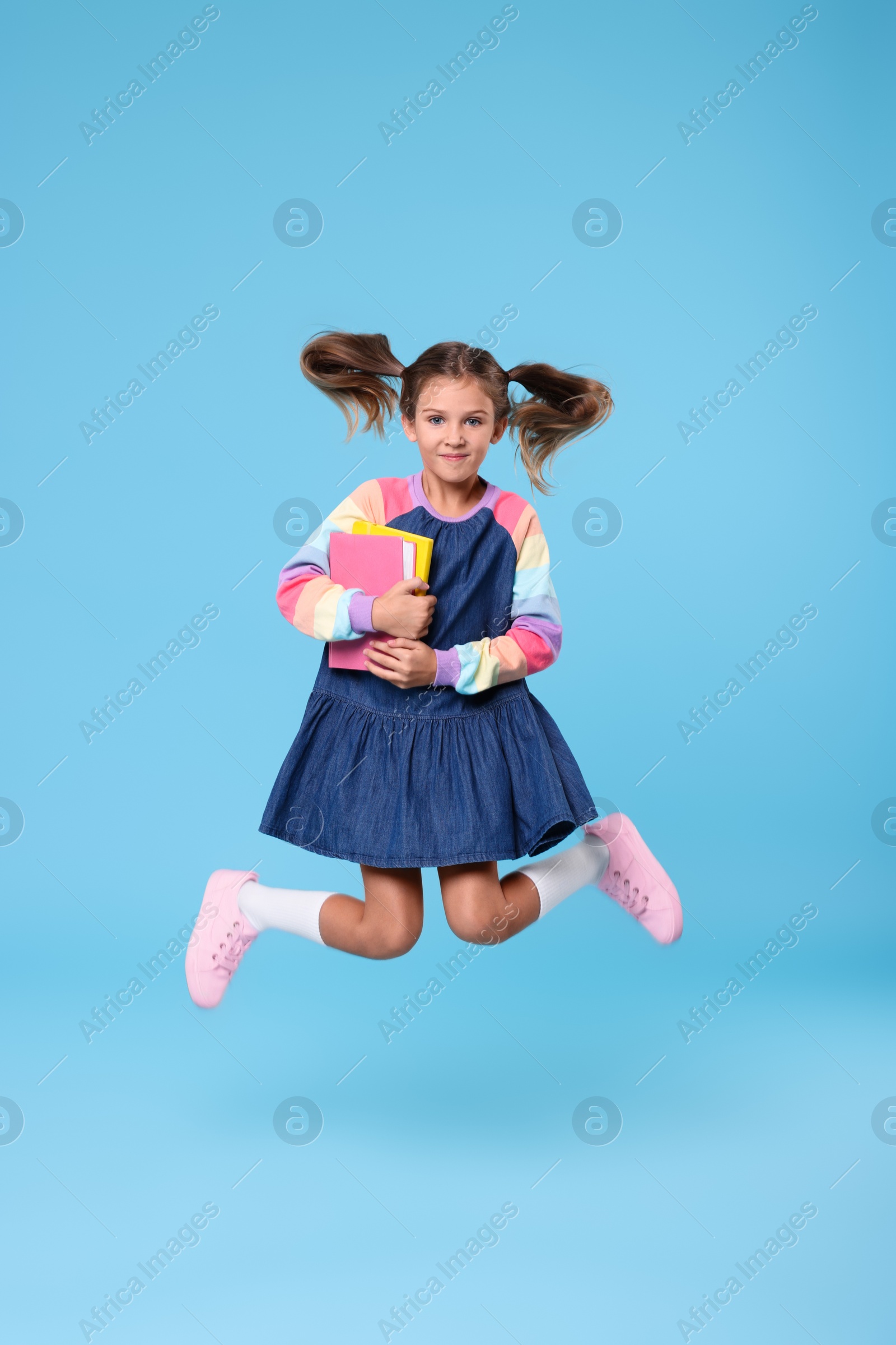 Photo of Cute schoolgirl with books jumping on light blue background
