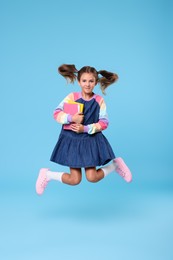Cute schoolgirl with books jumping on light blue background