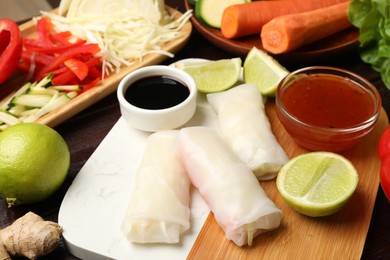 Photo of Delicious spring rolls with vegetables, lime and sauces on table, closeup