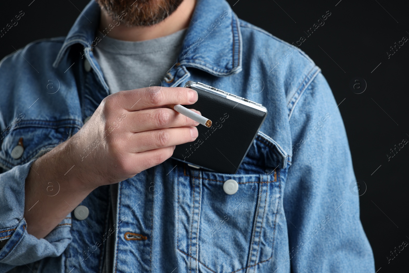 Photo of Man putting cigarette case into pocket on black background, closeup