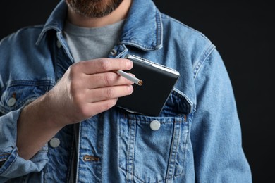 Photo of Man putting cigarette case into pocket on black background, closeup
