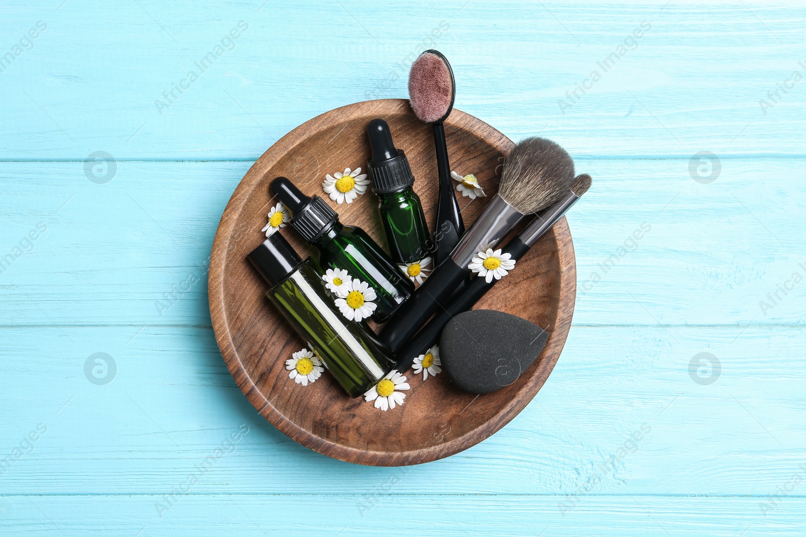 Photo of Chamomile flowers, cosmetic products and brushes on light blue wooden table, top view