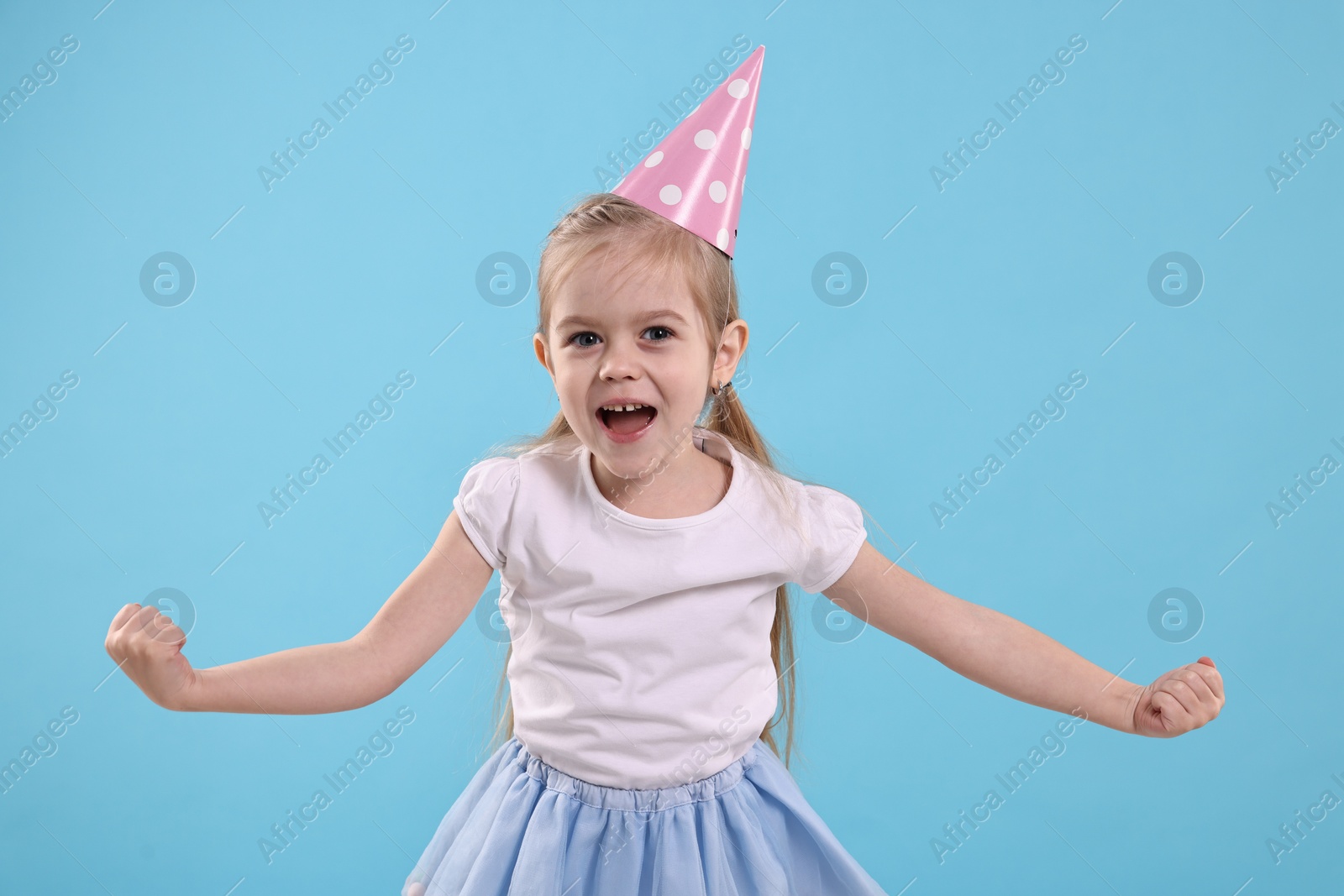 Photo of Birthday celebration. Cute little girl in party hat on light blue background