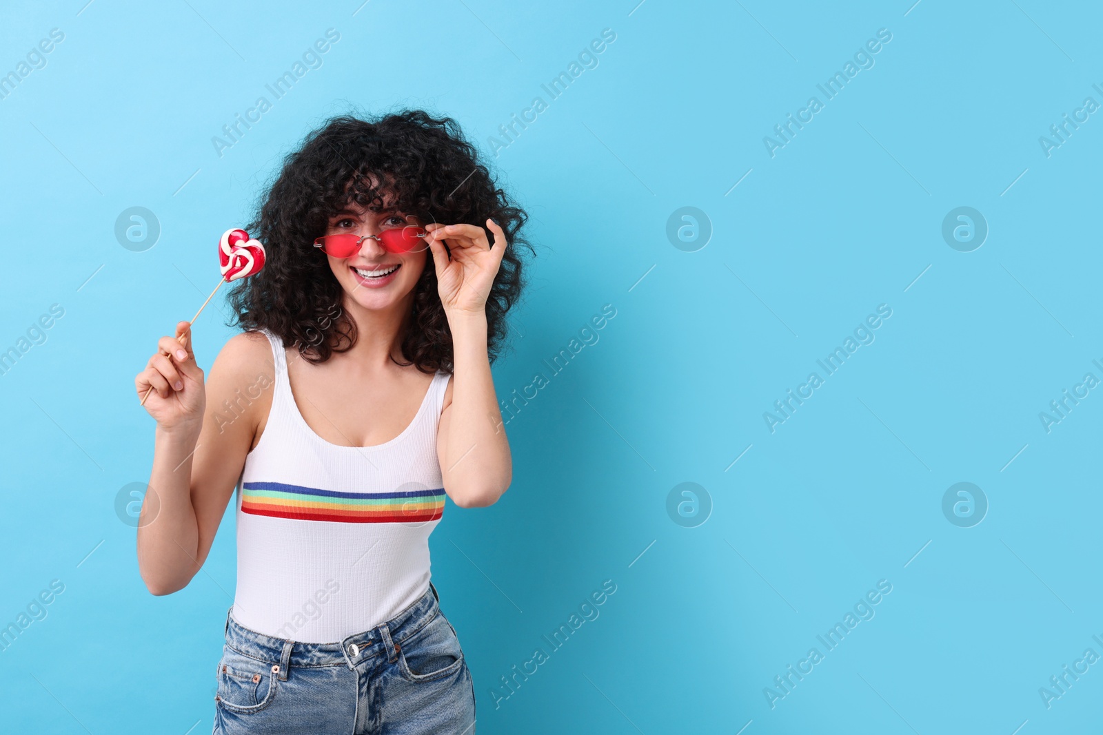 Photo of Beautiful woman in sunglasses with lollipop on light blue background, space for text