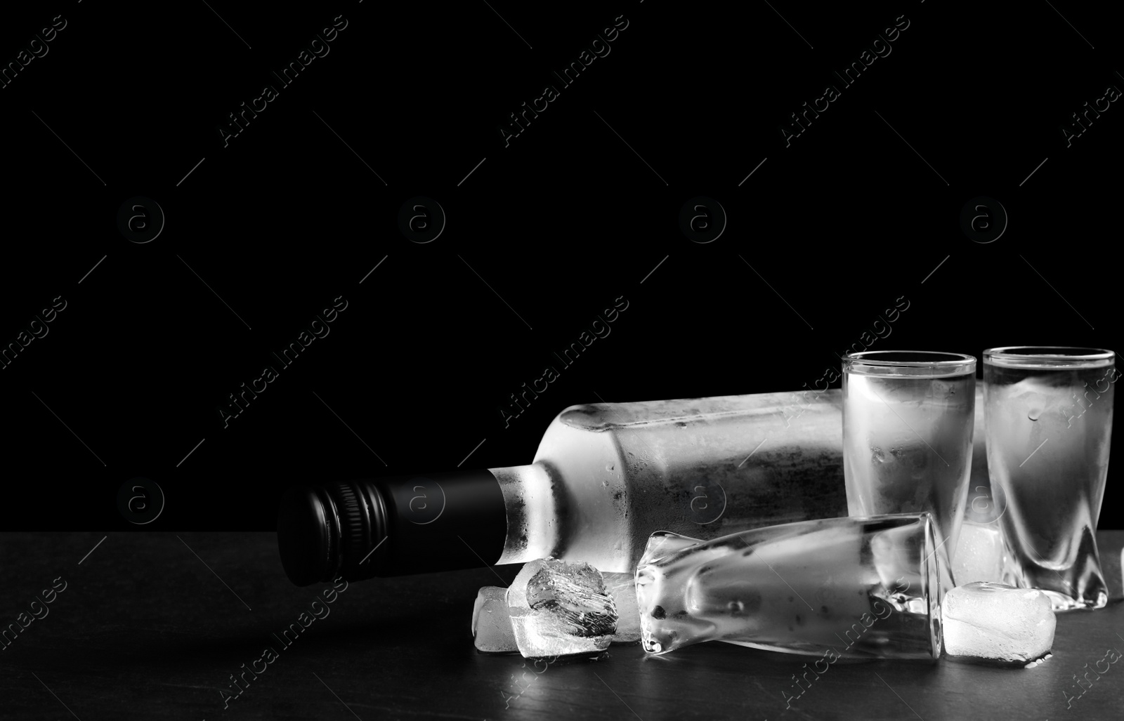 Photo of Bottle of vodka and shot glasses with ice on table against black background. Space for text