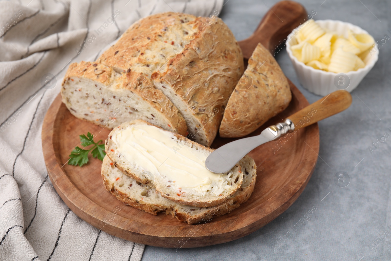 Photo of Tasty bread with butter and knife on grey textured table, closeup