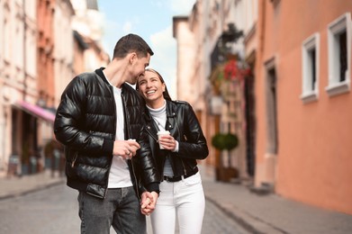 Photo of Lovely young couple with cups of coffee walking together on city street. Romantic date