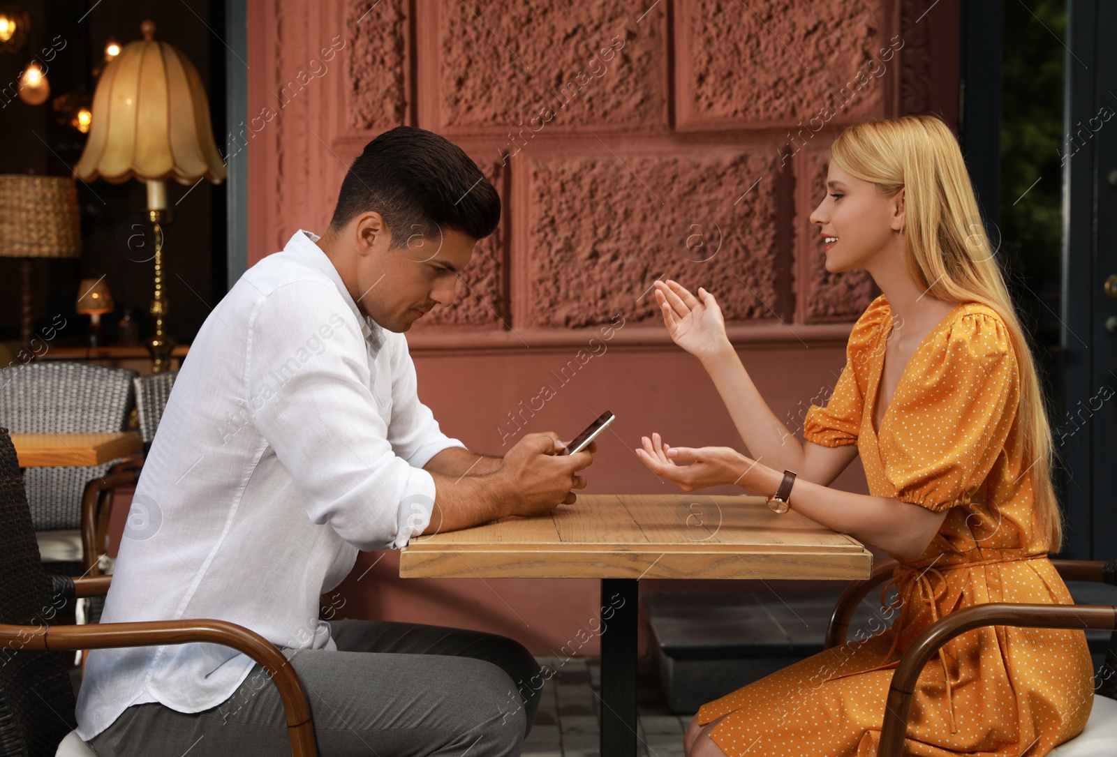 Photo of Man with smartphone ignoring his girlfriend in cafe. Boring date