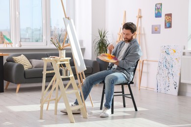 Photo of Man painting in studio. Using easel to hold canvas