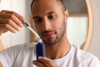 Handsome man with cosmetic serum in hands indoors