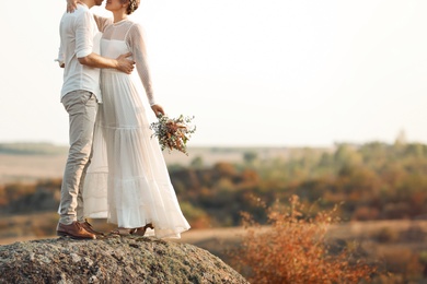 Happy newlyweds with beautiful field bouquet outdoors, closeup