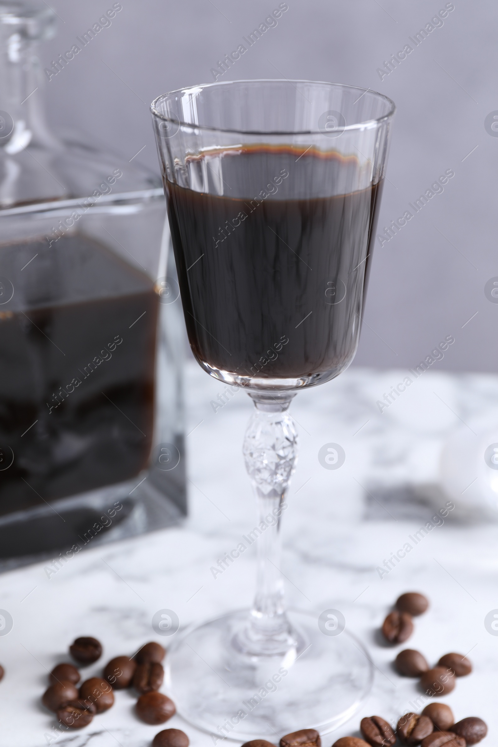 Photo of Coffee liqueur and beans on white marble table, closeup