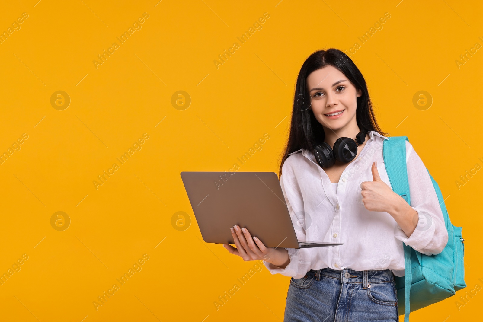 Photo of Smiling student with laptop showing thumb up on yellow background. Space for text
