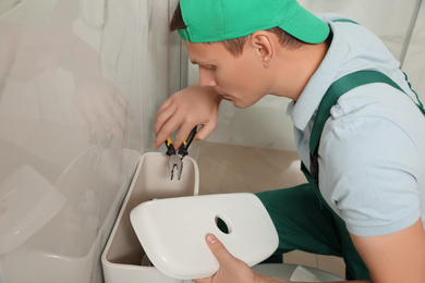 Photo of Professional plumber repairing toilet tank in bathroom