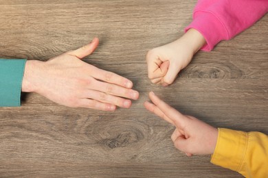 Closeup of people playing rock, paper and scissors on wooden background, top view