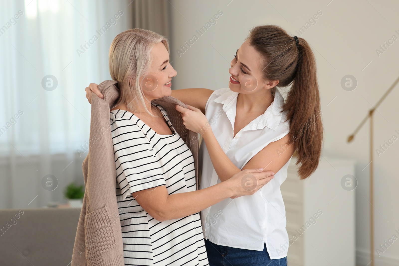 Photo of Young woman covering her mother with warm cardigan at home. Family help