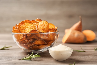 Delicious sweet potato chips in bowl, rosemary and sauce on table