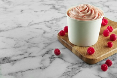 Cup with tasty frozen yogurt and raspberries on marble table. Space for text