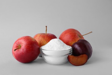 Photo of Bowl with sweet fructose powder, ripe apples and plums on white background