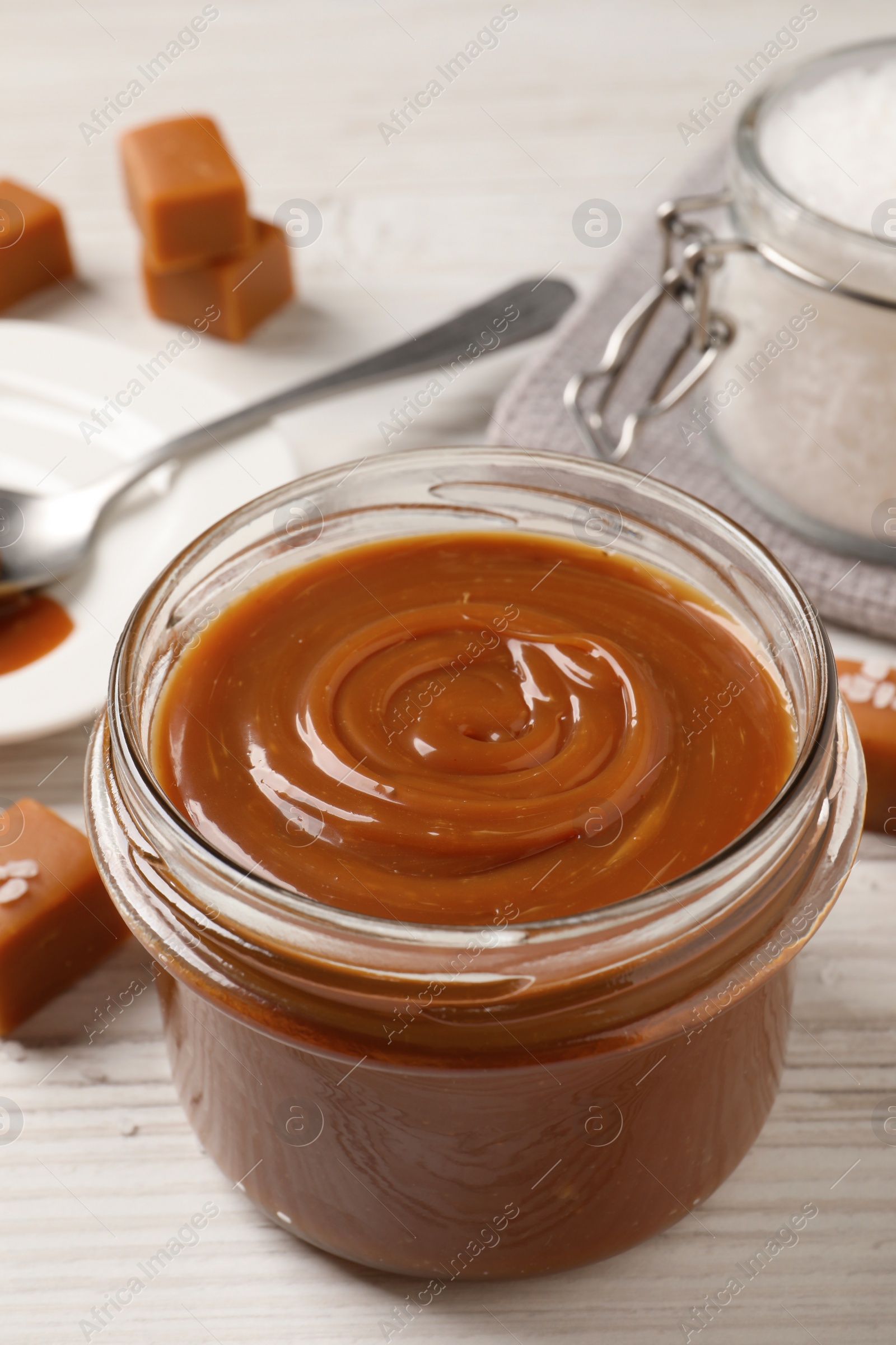 Photo of Yummy salted caramel in glass jar on white wooden table