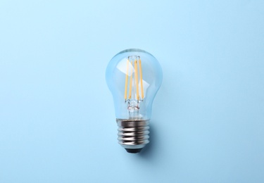 Photo of New modern lamp bulb on light blue background, top view