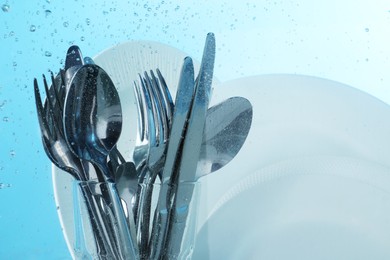 Photo of Washing silver cutlery and plates in water on light blue background
