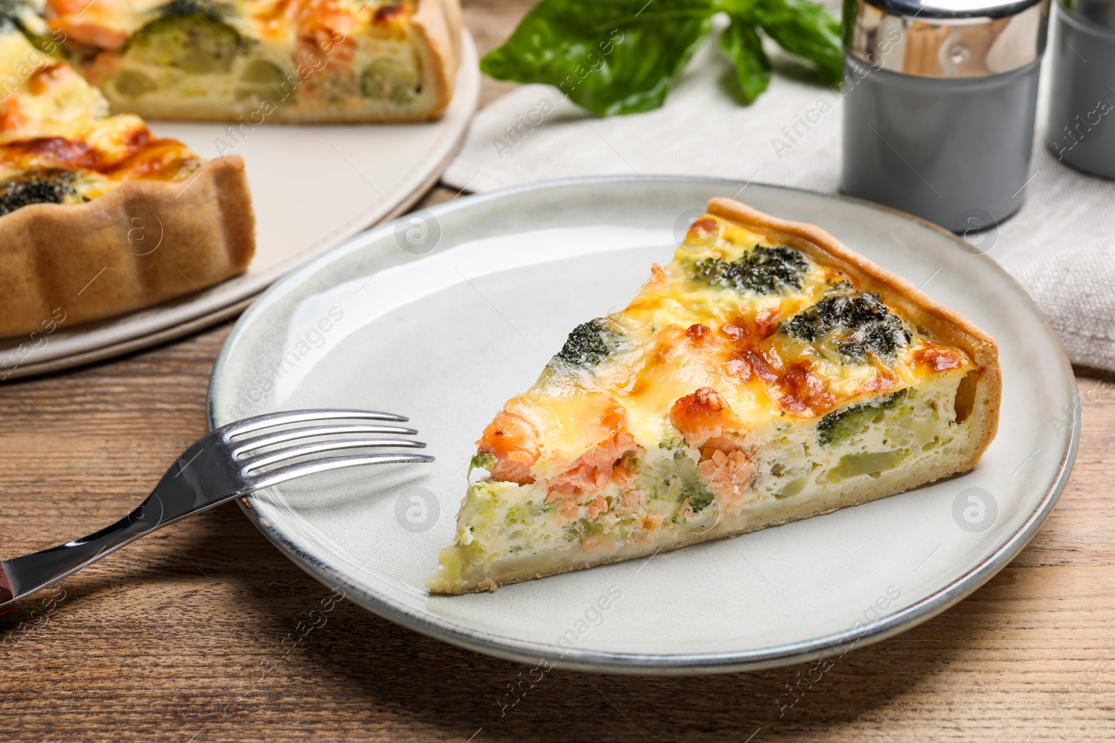 Photo of Piece of delicious homemade salmon quiche with broccoli and fork on wooden table