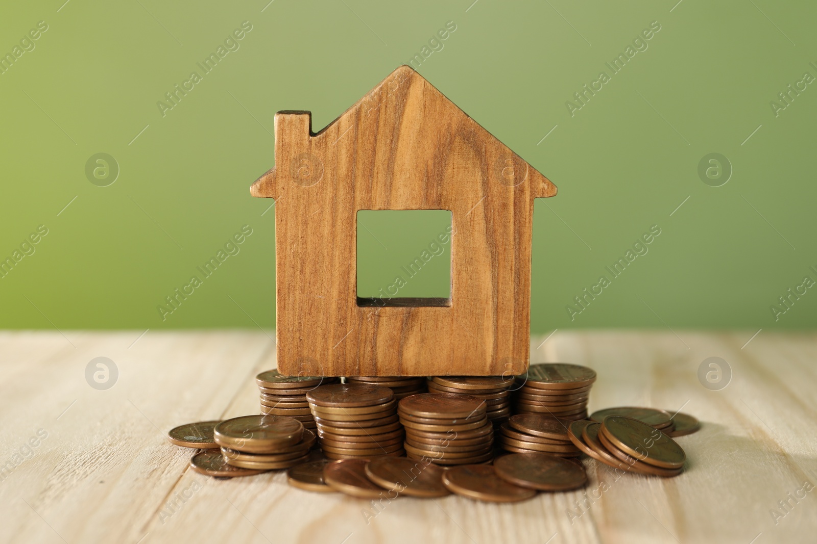 Photo of House model and coins on wooden table against green background