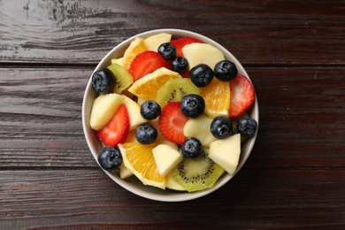 Tasty fruit salad in bowl on wooden table, top view