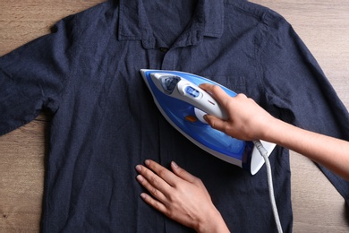 Woman ironing shirt on wooden background, top view