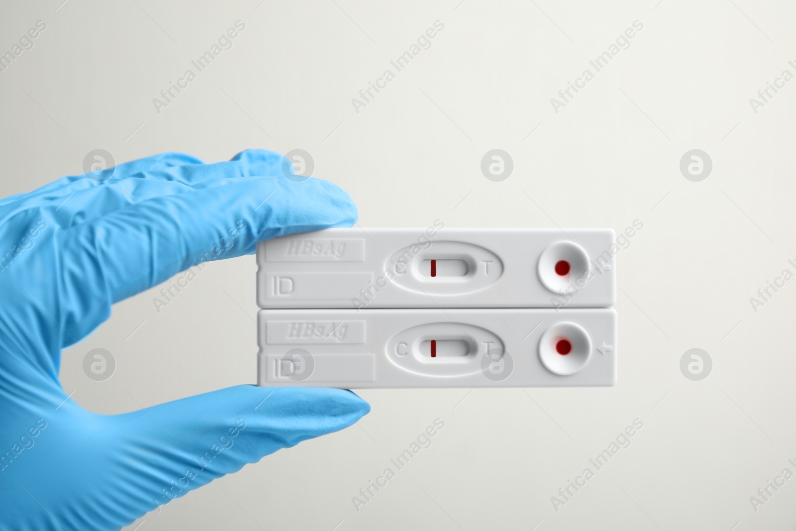 Photo of Doctor in gloves holding disposable express tests for hepatitis on white background, closeup