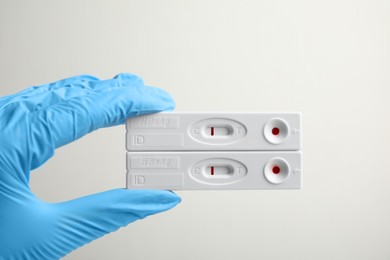 Photo of Doctor in gloves holding disposable express tests for hepatitis on white background, closeup