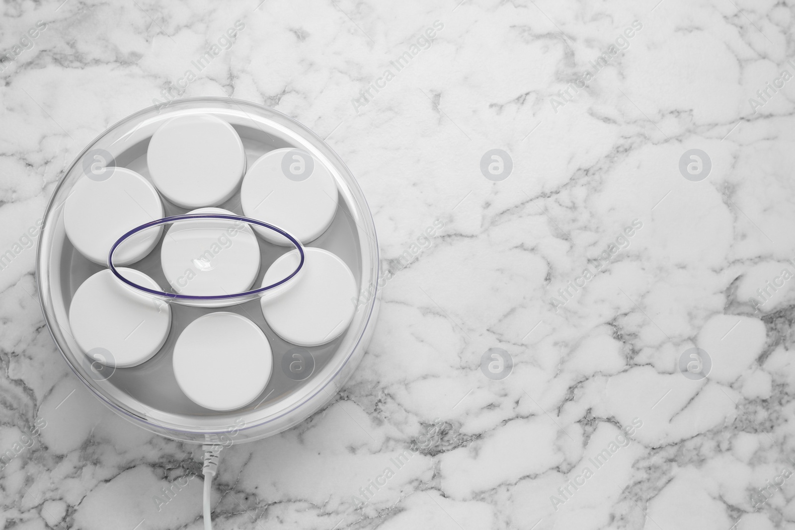 Photo of Modern yogurt maker with jars on white marble table, top view. Space for text