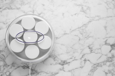 Modern yogurt maker with jars on white marble table, top view. Space for text