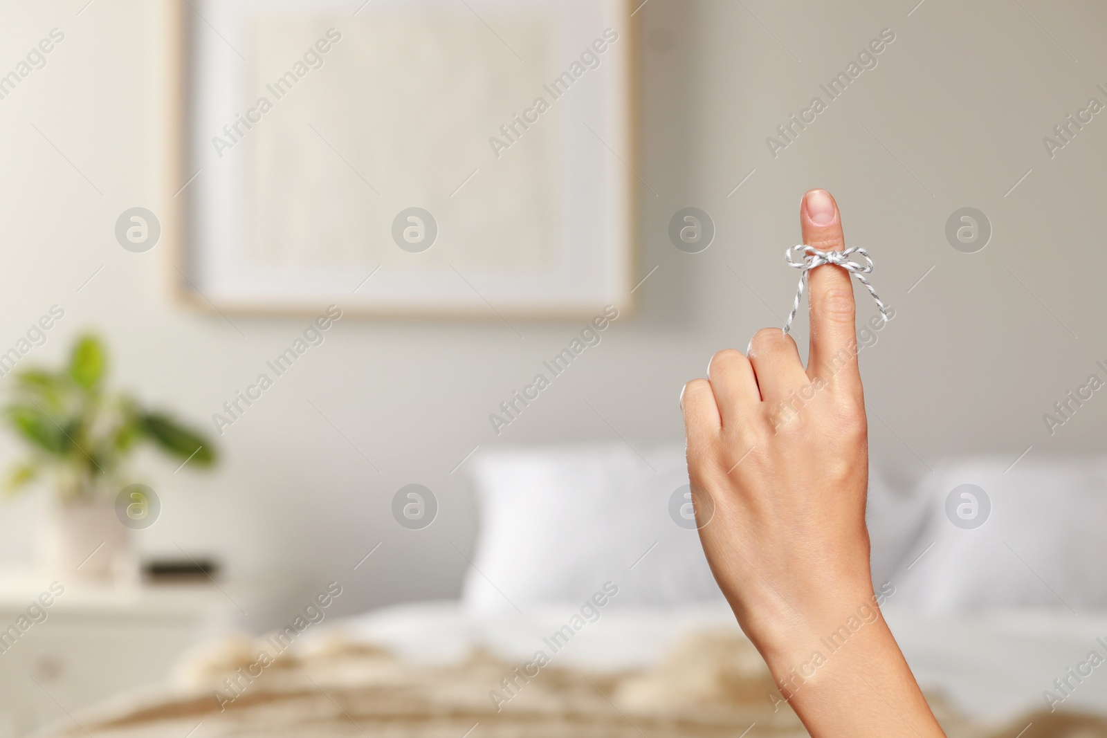 Photo of Woman showing index finger with tied bow as reminder indoors, closeup. Space for text