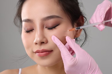 Woman getting facial injection on grey background, closeup