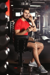 Young man with headphones listening to music on mobile device at gym