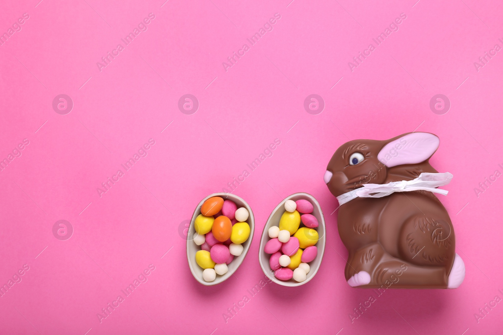 Photo of Chocolate Easter bunny, halves of egg and candies on pink background, flat lay. Space for text