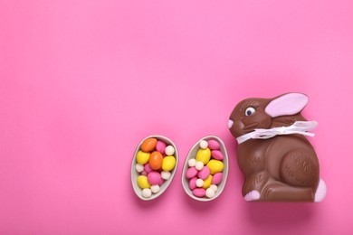 Photo of Chocolate Easter bunny, halves of egg and candies on pink background, flat lay. Space for text