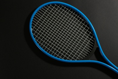 Tennis racket on black background, top view. Sports equipment